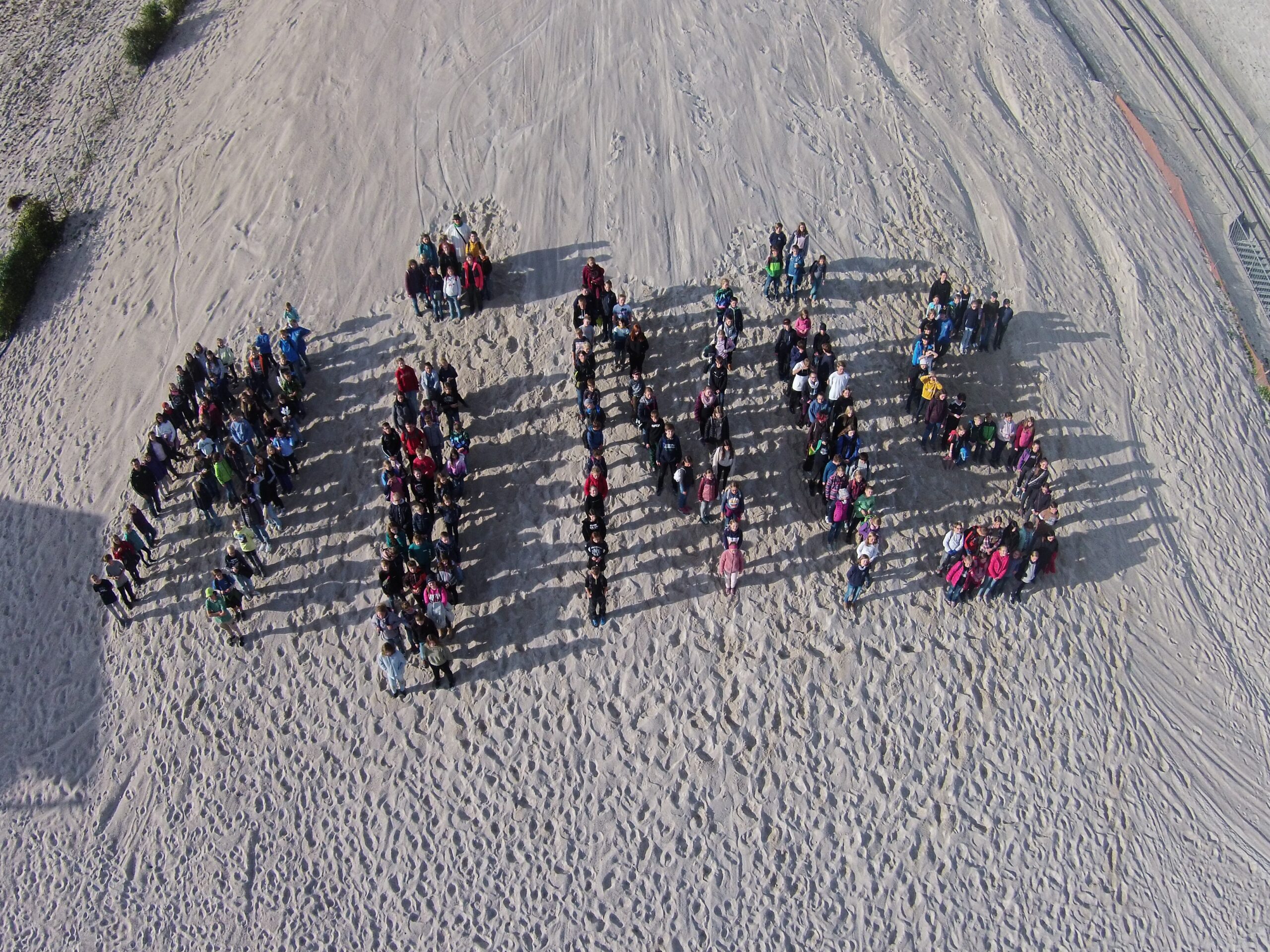 Man sieht Ministranten im Sand stehen, die mit das Wort "Minis" formen
